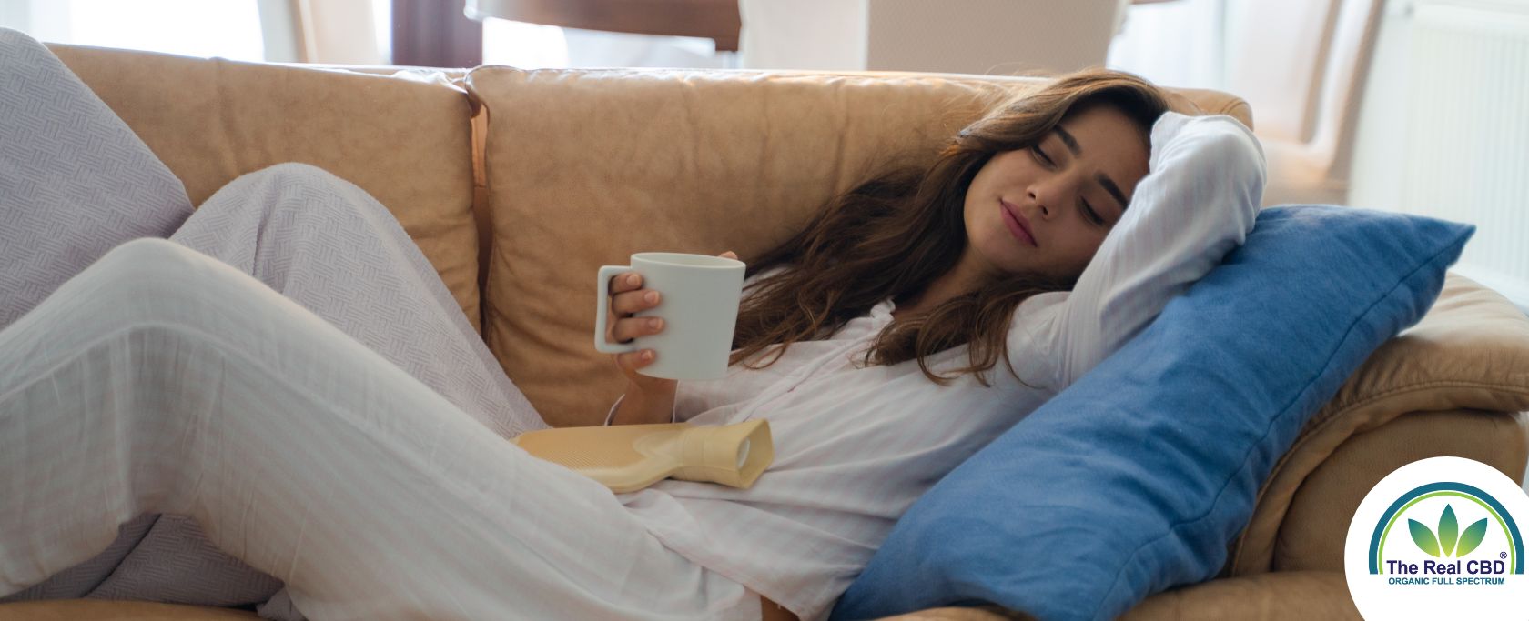 Kvinde ligger på en sofa og drikker af et hvidt krus