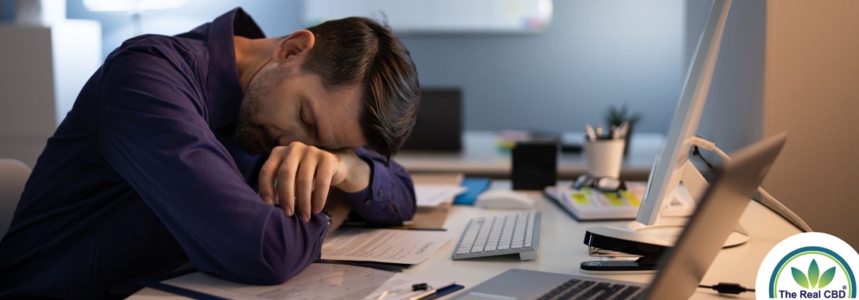 Mand sover ved et kontorbord med flere computere