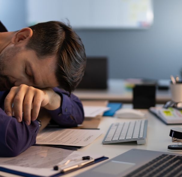 Mand sover ved et kontorbord med flere computere