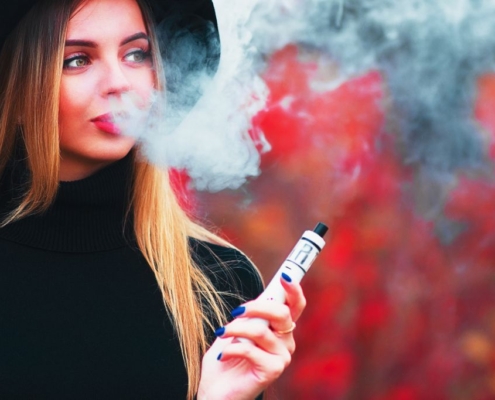Ung smuk kvinde i ryggen blæser vape-røg på en rød baggrund