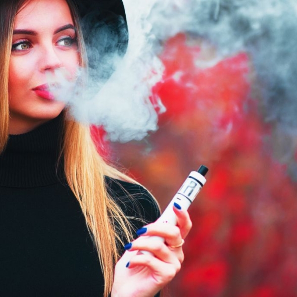 Ung smuk kvinde i ryggen blæser vape-røg på en rød baggrund