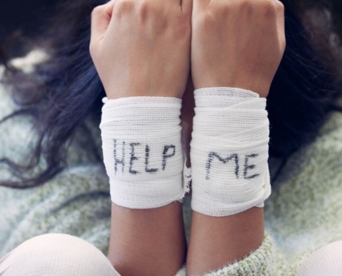 Kvinde med bandager om håndleddene, der staver HELP ME