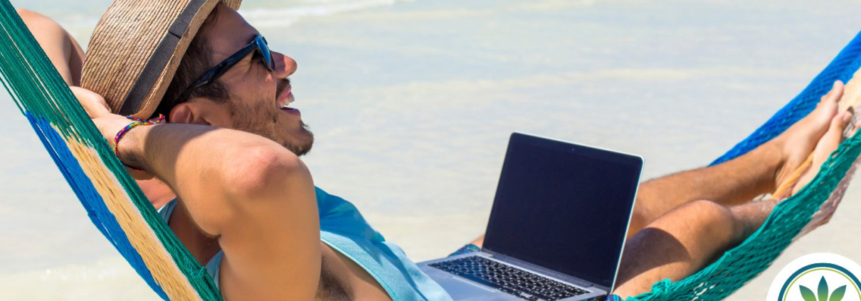 En mand ligger i en hængekøje på stranden med sin bærbare computer på skødet.