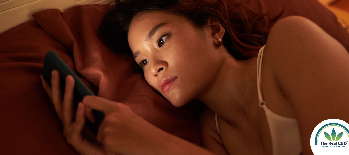 Kvinde ligger og scroller på sin telefon om natten under dynen