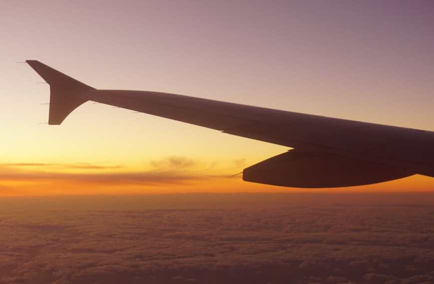 Vingen på et fly, der flyver mod solopgangen