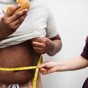 Hombre comiendo una hamburguesa mientras le miden la cintura