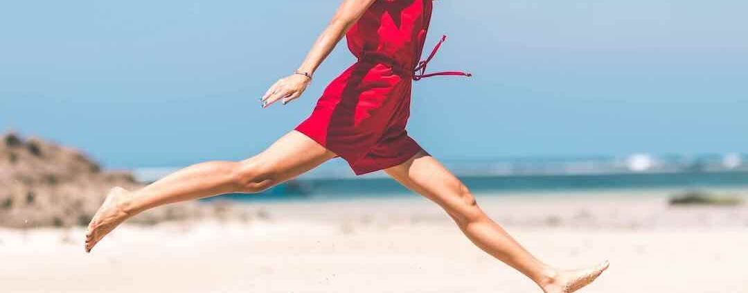 Mujer con vestido rojo saltando en la playa