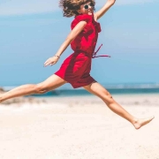 Mujer con vestido rojo saltando en la playa