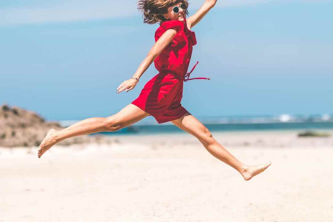 Mujer con vestido rojo saltando en la playa