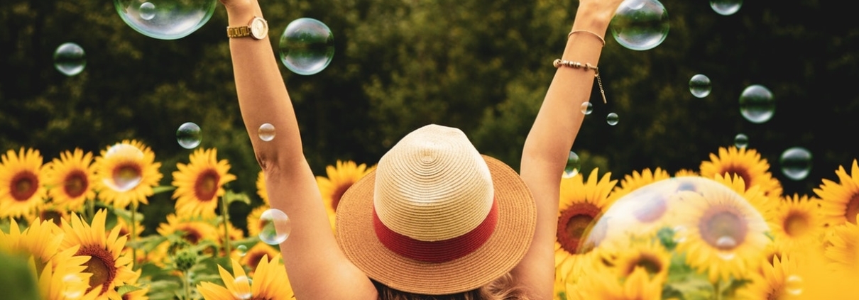 Mujer con sombrero de verano en campo de girasoles haciendo burbujas