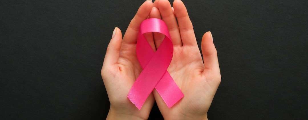 Manos femeninas sosteniendo un lazo rosa contra el cáncer