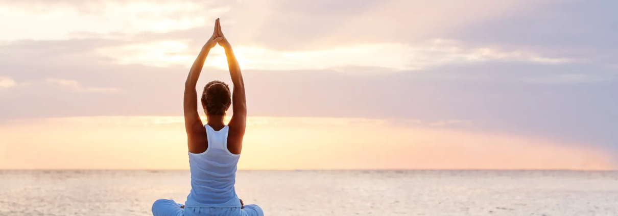 Mujer en postura de yoga junto al mar al amanecer