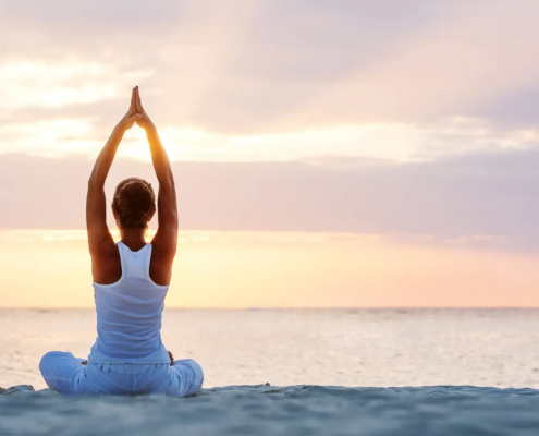 Mujer en postura de yoga junto al mar al amanecer