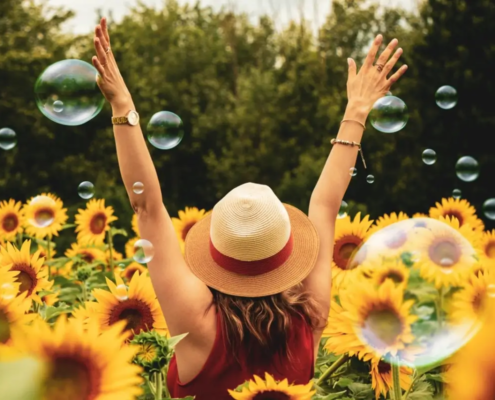 Mujer con sombrero de verano en un campo de girasoles, levantando los brazos entre burbujas en el aire