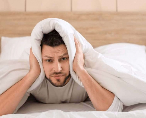 Hombre en la cama tapándose los oídos