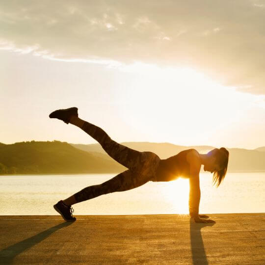 Mujer al atardecer haciendo planking en el suelo