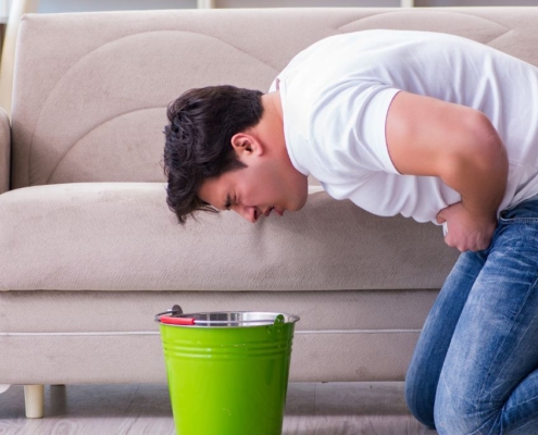 Hombre vomitando en un cubo verde