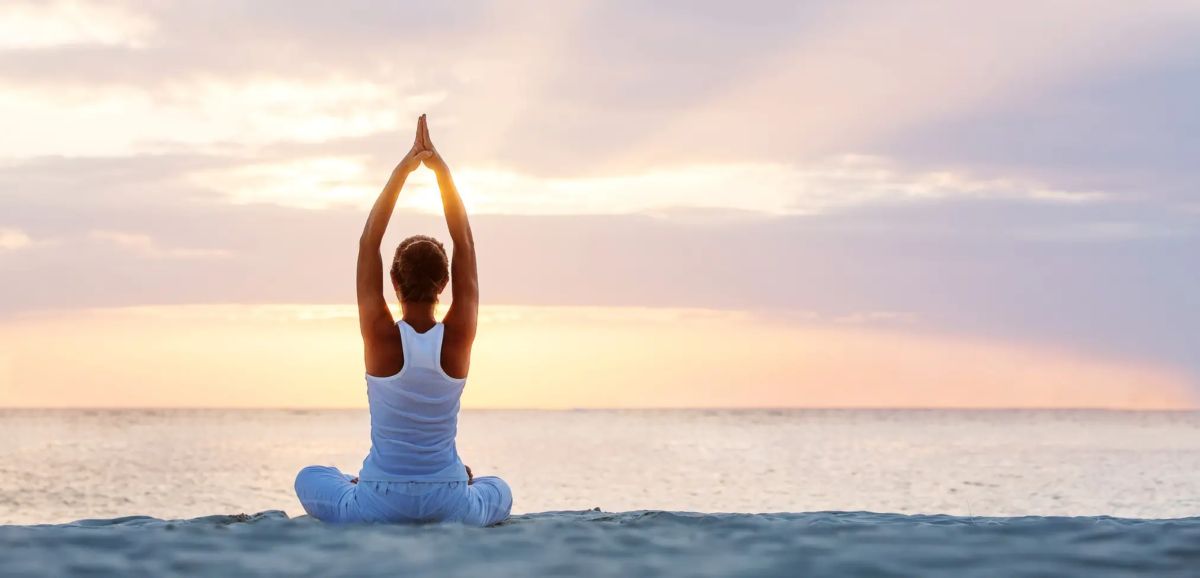 Mujer en postura de yoga sentada en una playa al amanecer