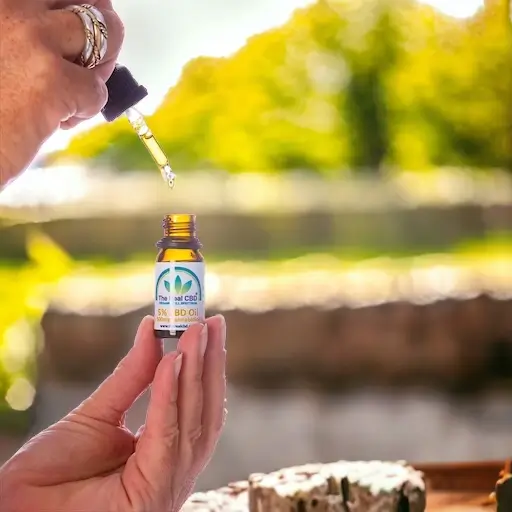 Mano que sostiene una tintura de CBD abierta en un campo - The Real CBD Marca