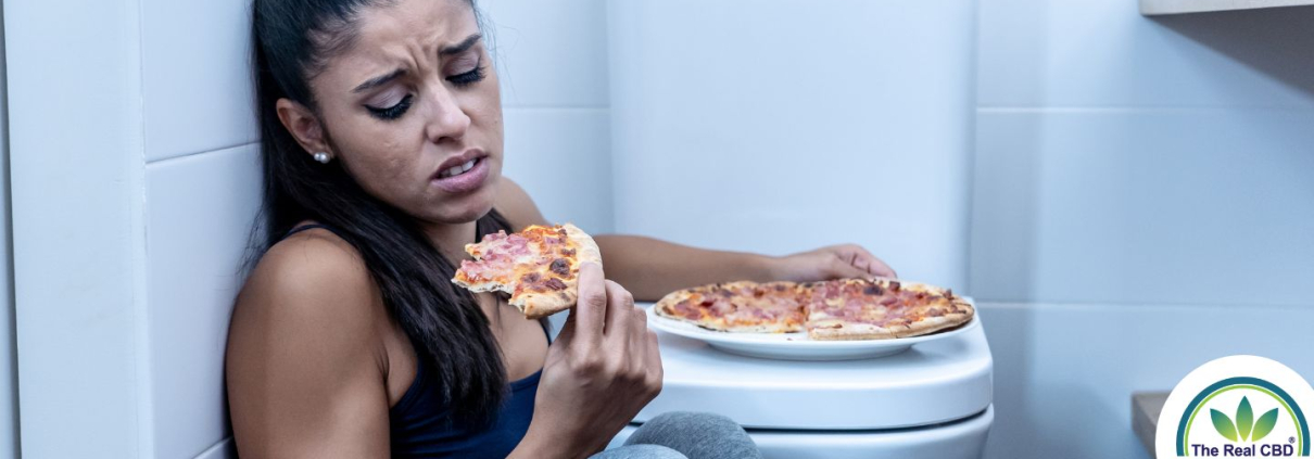 Mujer sentada en el suelo del baño comiendo pizza junto al váter