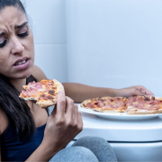 The-Real-CBD-blog-CBD para los trastornos alimentarios Mujer sentada en el suelo del baño comiendo pizza junto al váter
