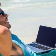 the-real-cbd-blog-CBD-para-nómadas-digitales Hombre en una hamaca en la playa con su ordenador portátil trabajando bajo el sol.