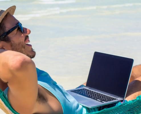 Hombre en una hamaca en la playa con su ordenador portátil trabajando bajo el sol.
