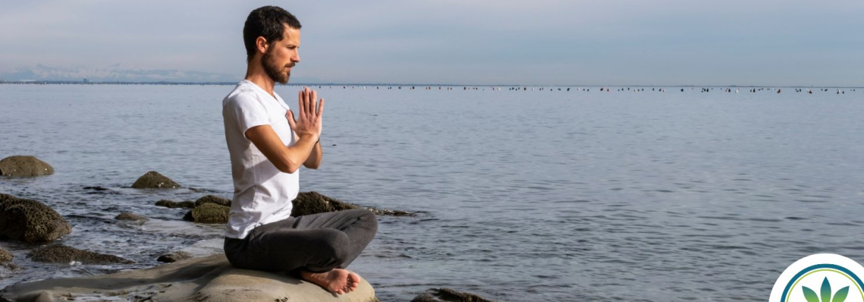 Hombre sentado junto al mar haciendo ejercicios de respiración.