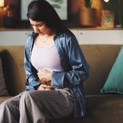 The-Real-CBD-Blog-aceite-de-CBD-para-el-malestar-digestivo-y-la-hinchazón Mujer sentada en el sofá sujetándose el estómago con dolor.