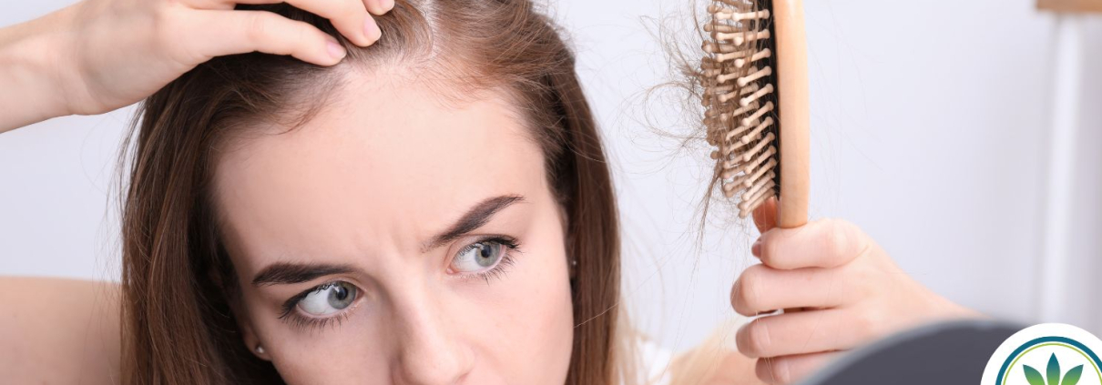 Una mujer que parece asustada al ver su cepillo lleno de pelo y la calva que tiene en la frente