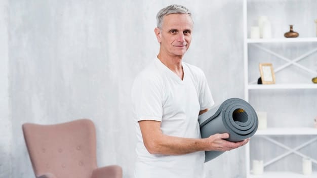 smiling-old-man-standing-home-with-rolled-yoga-mat