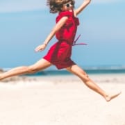 Der-Real-CBD-Blog-Kann-CBD-bei-Fibromyalgie-helfen Frau im roten Kleid springt glรผcklich am Strand