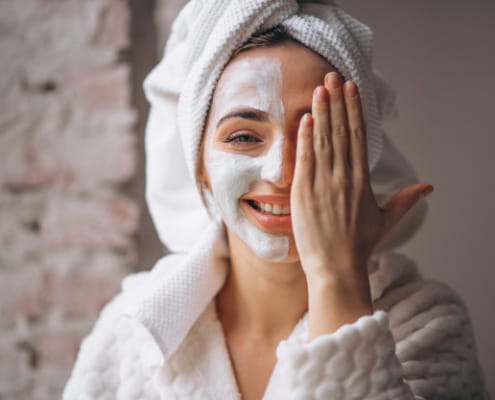 Lächelnde Frau im Hausmantel mit einer Gesichtsmaske auf einer Seite ihres Gesichts