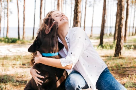 2512680 Femme souriante serrant son chien dans ses bras dans une forêt