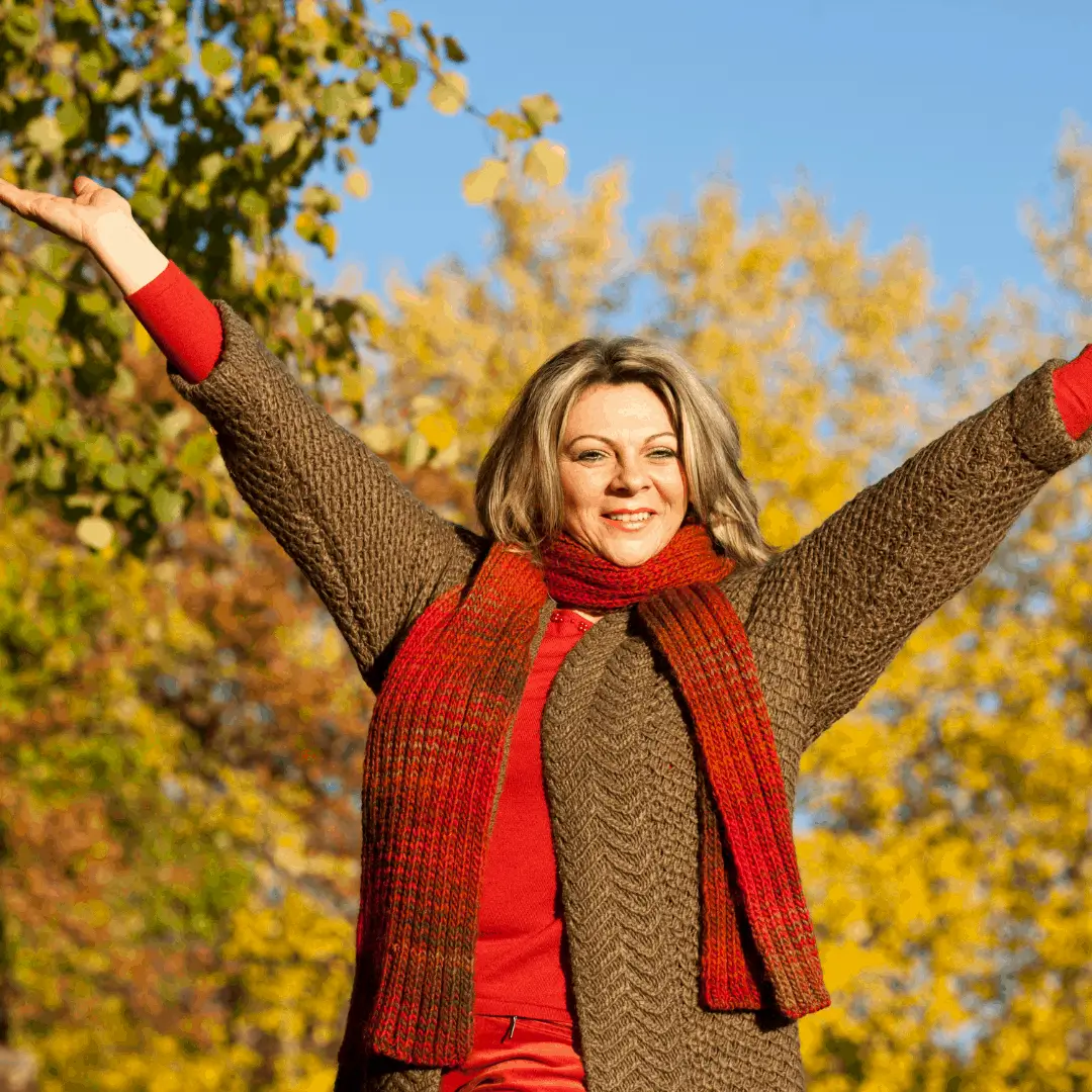 Happy woman in an autumn forest, rising her arms in content