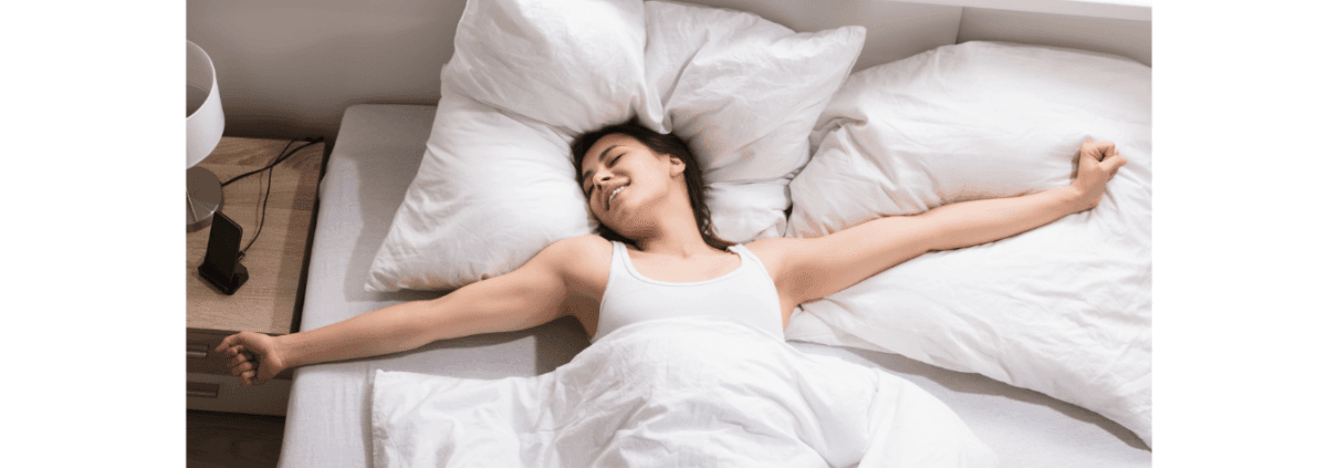 Lächelnde Frau, die in einem Bett mit weißen Laken aufwacht