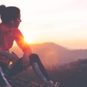 Der-Real-CBD-Blog-CBd-Heilungsbalsam-1 Läuferin sitzt auf einem Berggipfel und blickt in den Sonnenuntergang