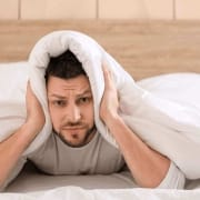 Der-Real-CBD-Blog-Kann-CBD-helfen-Tinnitus zu behandeln (1) (1) (1) (1) Mann unter der Bettdecke hält sich die Ohren zu