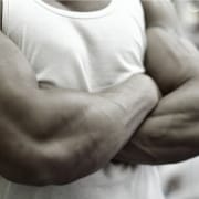 The-Real-CBD-Blog-CBD-รl-fรผr-besseren-Muskelaufbau-Stamina-und-Fitness Muskulรถser Mann in weiรem T-Shirt, der seine Arme verschrรคnkt
