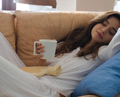 Vrouw liggend op een sofa drinkend uit een witte mok