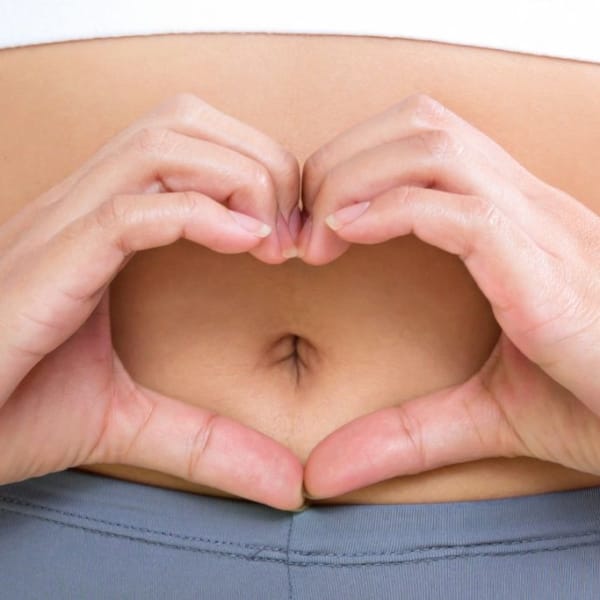 Vrouw maakt hartvorm met haar handen voor haar navel