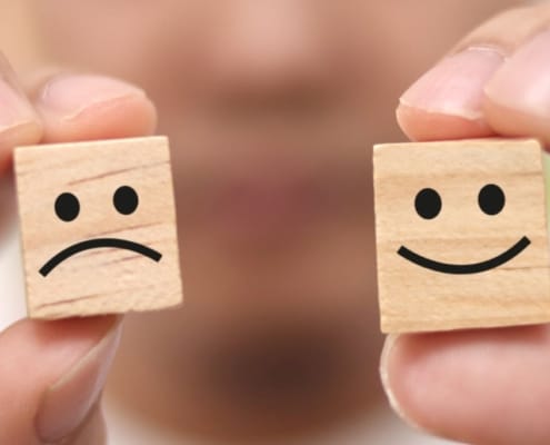 Hands holding happy and sad faced wooden cubes