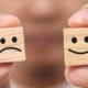 Hands holding happy and sad faced wooden cubes