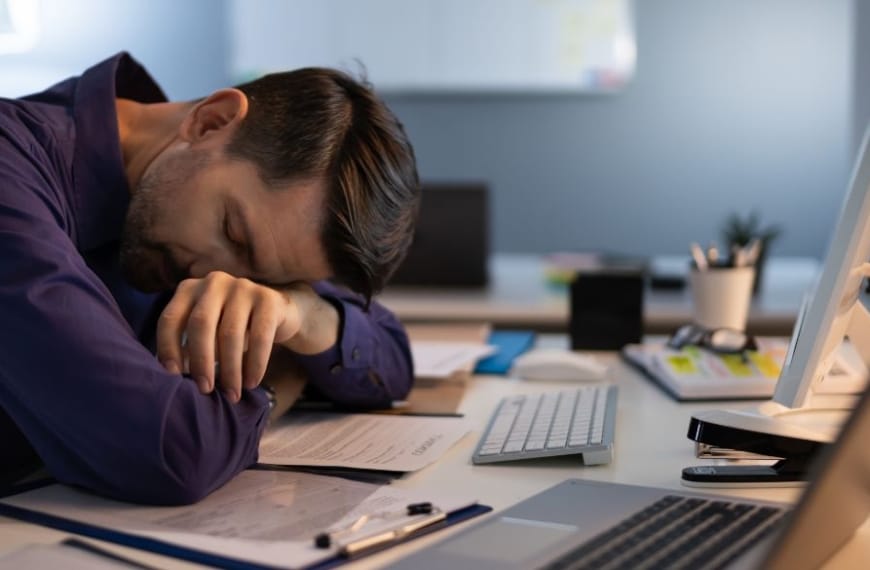 Mann schläft an einem Bürotisch mit mehreren Computern