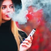 The-Real-CBD-Blog-Bénéfices-og CBD-vaping Jeune femme jolie de dos soufflant de la fumée de vapotage sur fond rouge