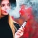 Jonge mooie vrouw op de rug blaast vape rook op een rode achtergrond