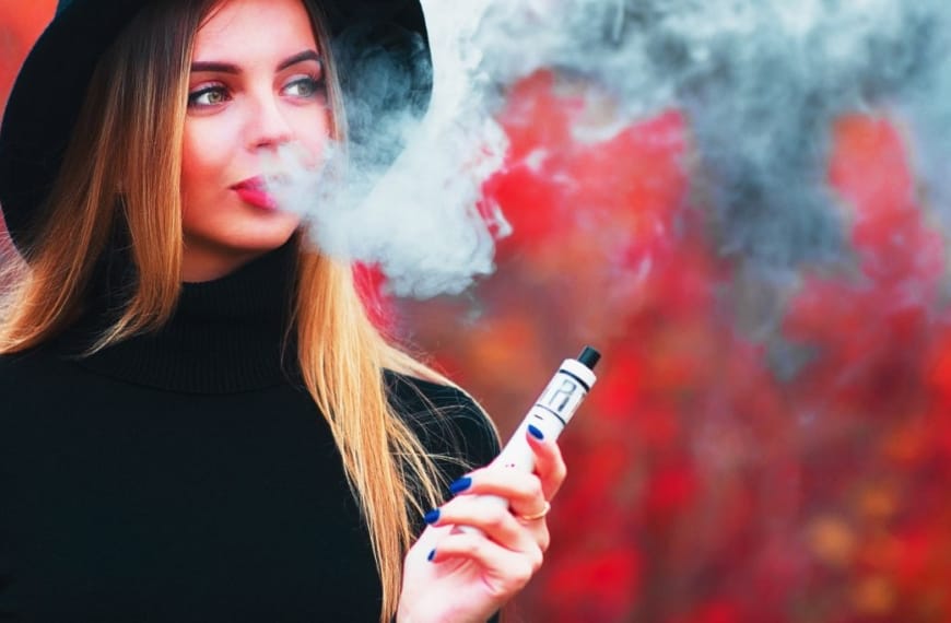 Young pretty woman in back blowing vape smoke on a red background