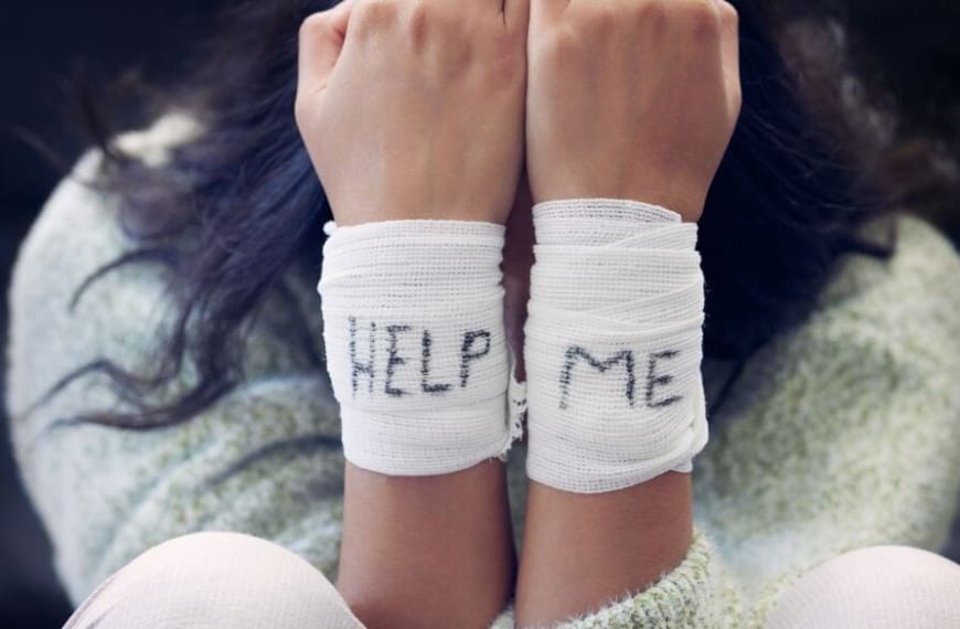 Woman with bandages on her wrists spelling HELP ME