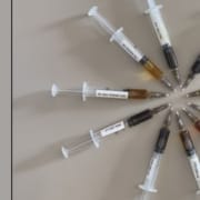 Der Real CBD Blog Decaboxyliertes oder rohes CBD 10 kreisförmig angeordnete Spritzen, die verschiedene Farben von CBD-Öl zeigen