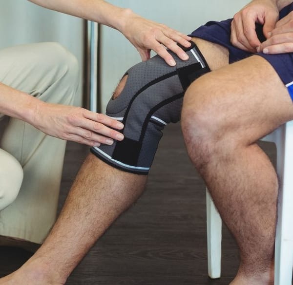 Verpleegster die zieke knie van zittende patiënt vasthoudt